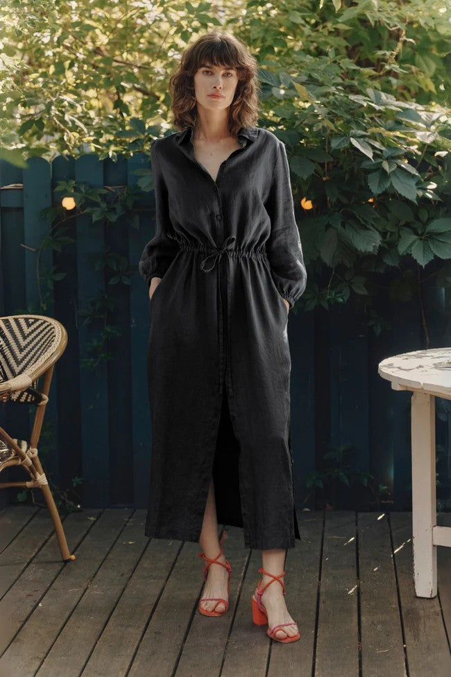 a confident woman in a black linen rhapsody dress posing with her dog on a city street