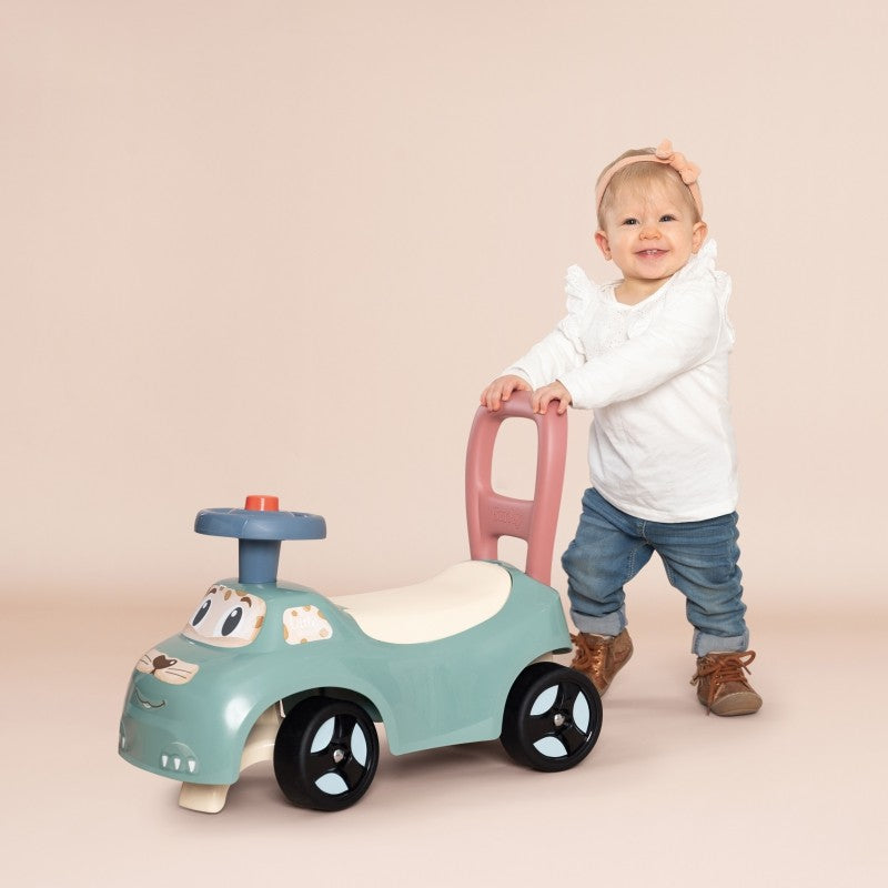 pastel blue ride-on pusher with horn and storage, seen from a low angle on a sunny patio, highlighting its sturdy wheels and ergonomic handle