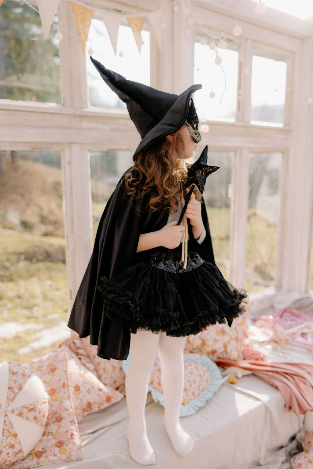 a young sorceress in a handmade black velour cape, the deep hood framing her face in a soft, magical light