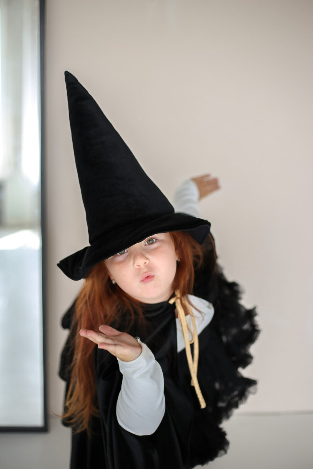 a young sorceress in a handmade black velour cape, the deep hood casting a mysterious shadow across her face