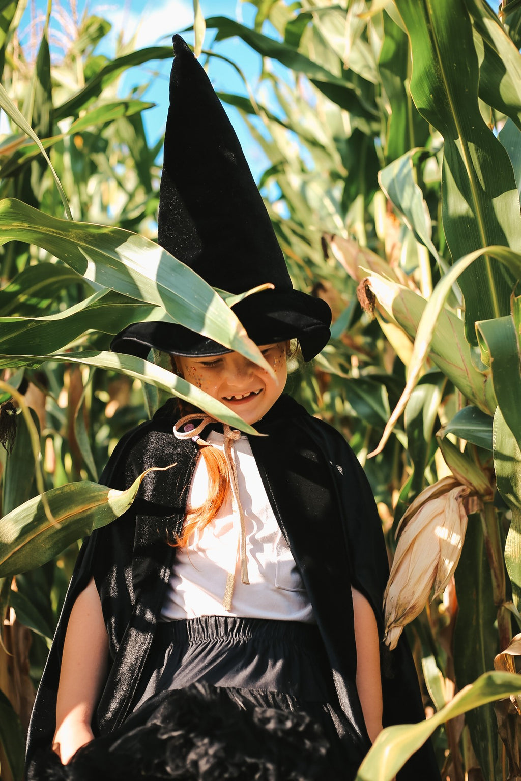 handmade black velour riding hood cape with a deep hood and snap fastening, shown in soft light