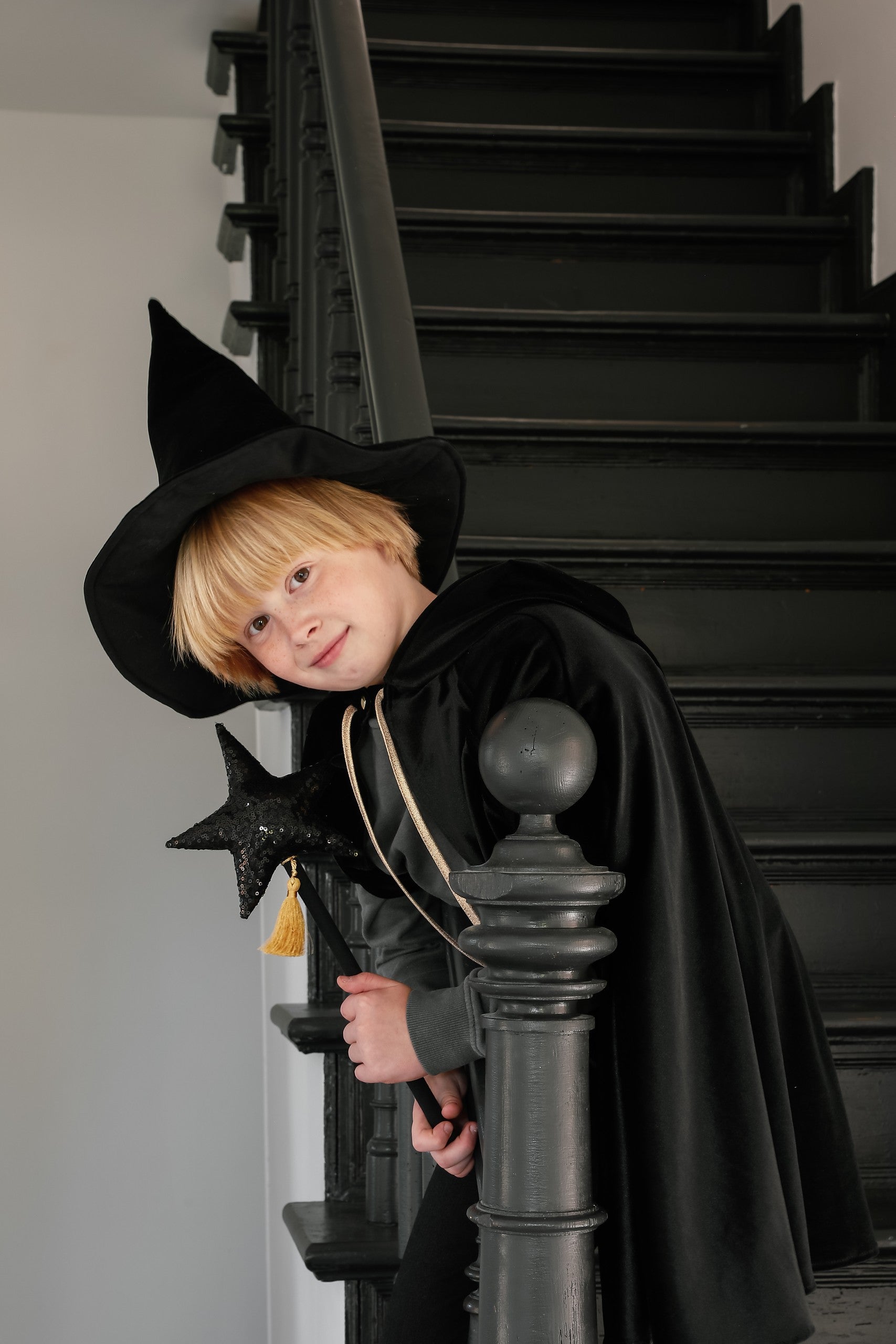child in a black velour hooded cape twirling in a sunlit garden adventure