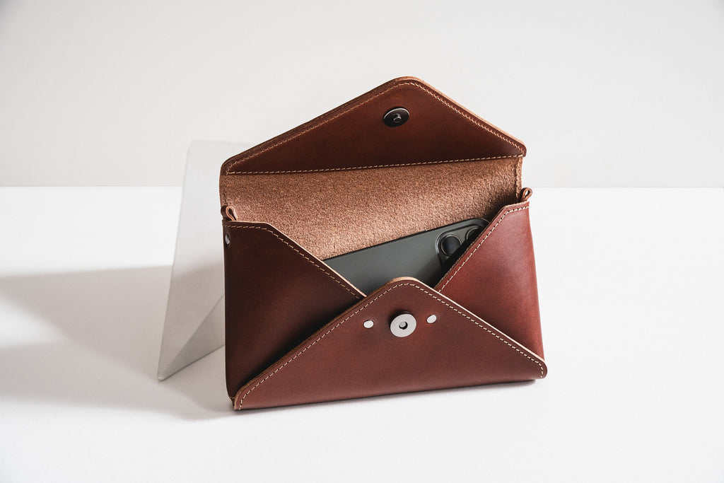 soft cognac leather mini clutch held gently in hand, showing its compact envelope shape and comforting texture
