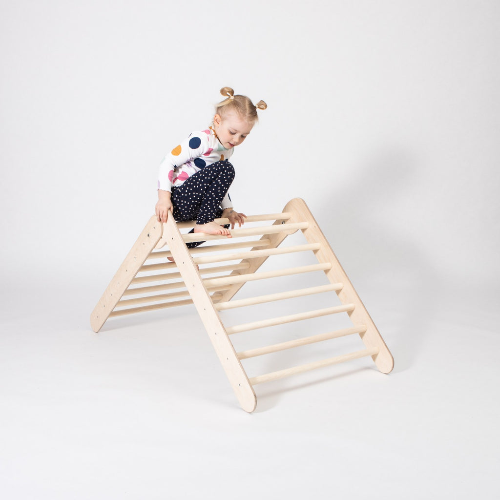 a soft-lit view of a child's hands gently gripping the birch rungs of a montessori climbing triangle