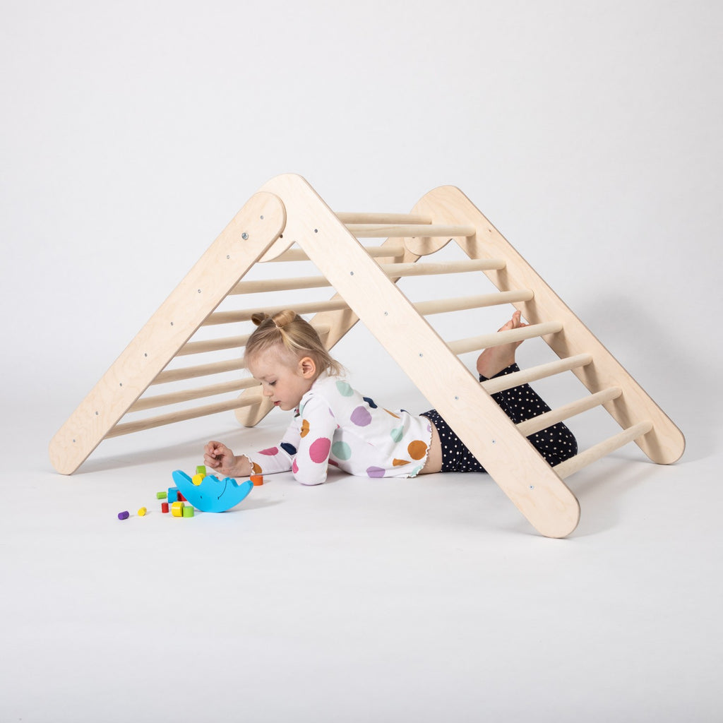 bold low-angle shot of a toddler confidently climbing the montessori triangle gym