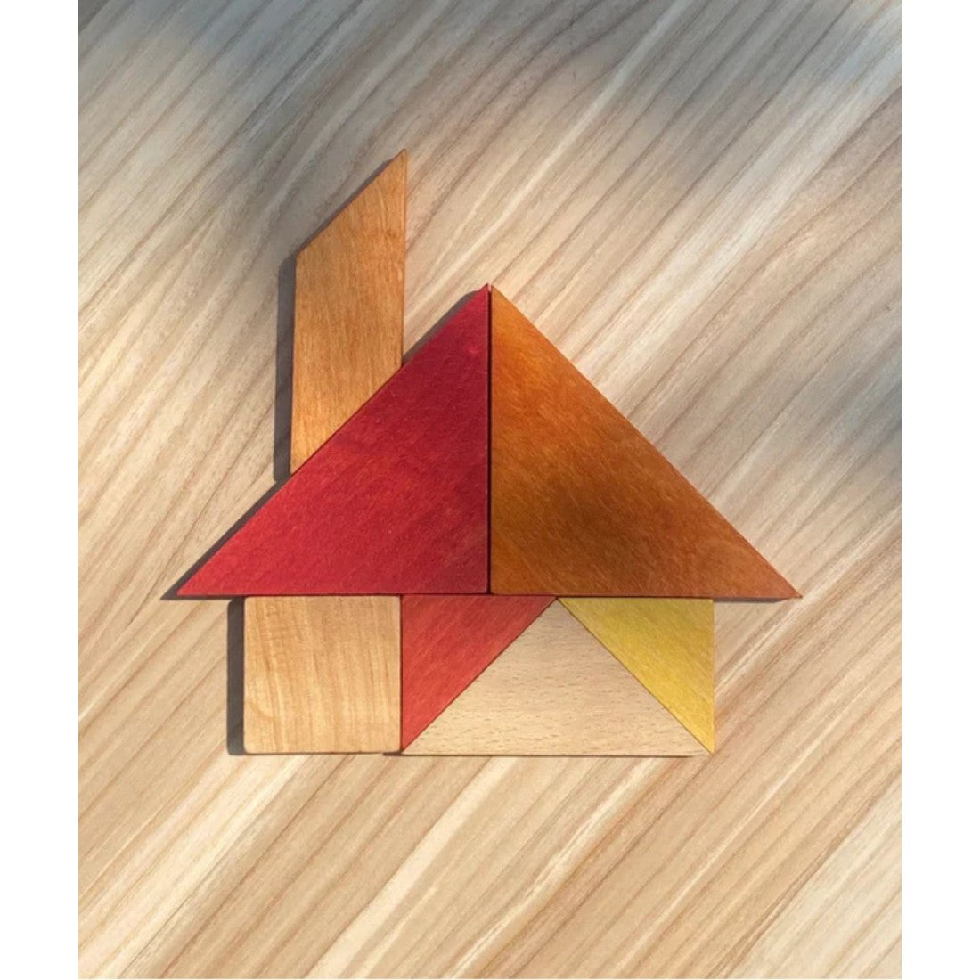 a soft-focus close-up of the warm-toned wooden tangram pieces resting gently on their leather travel bag