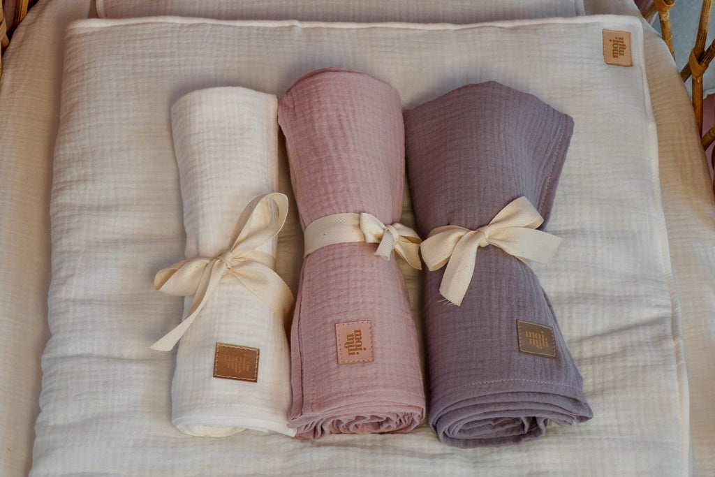 playful cream muslin baby blanket and pillow set draped over a wooden rocking chair, ready for naptime cuddles