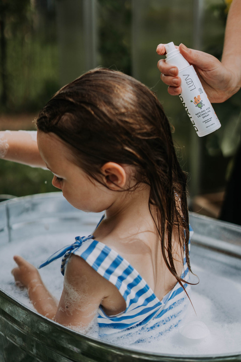 gentle kid's detangler spray with a soft pear scent, held in a comforting morning light