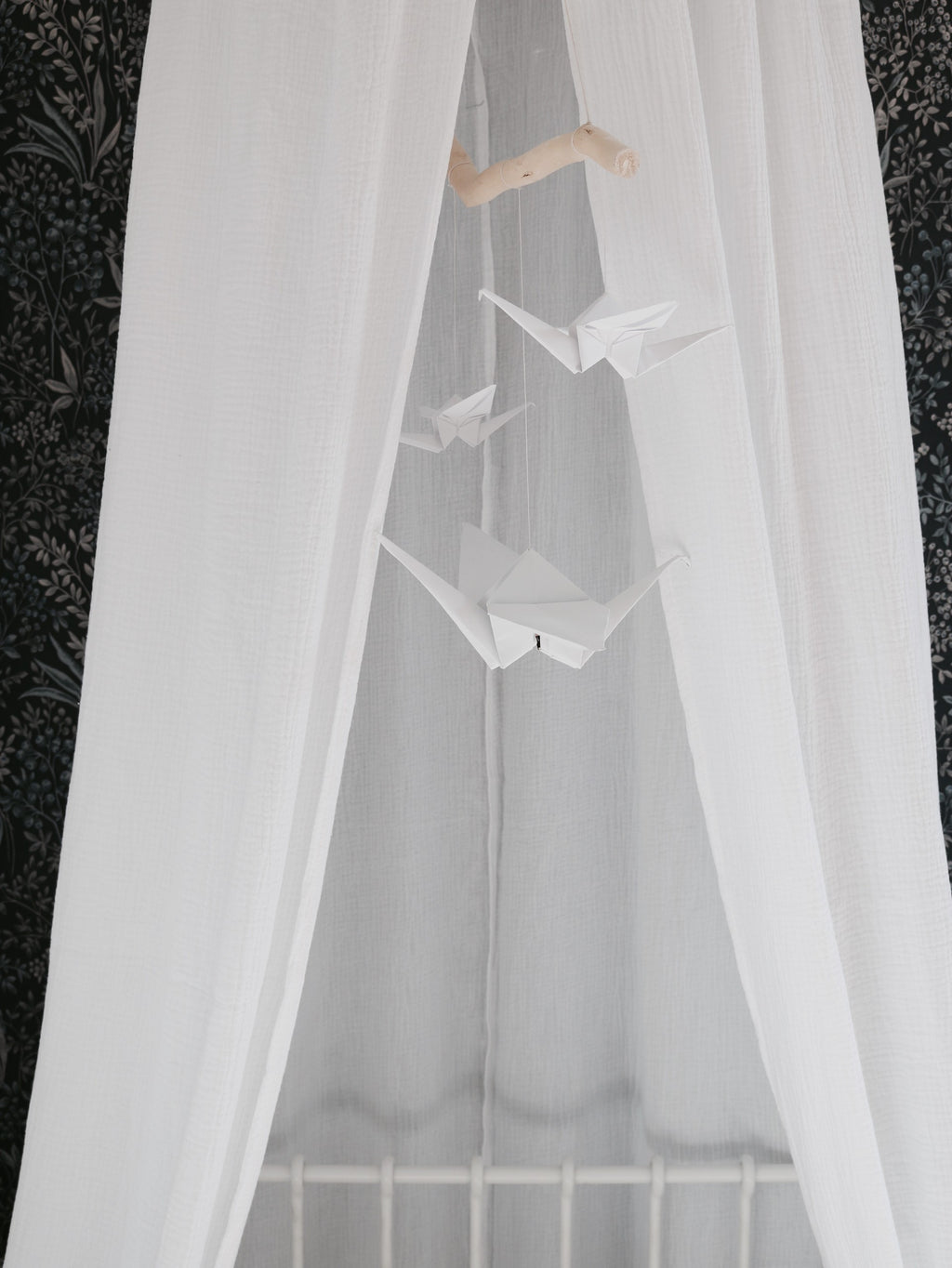 bold white origami nursery mobile with delicate cranes and pompoms, hanging above a crib in soft daylight