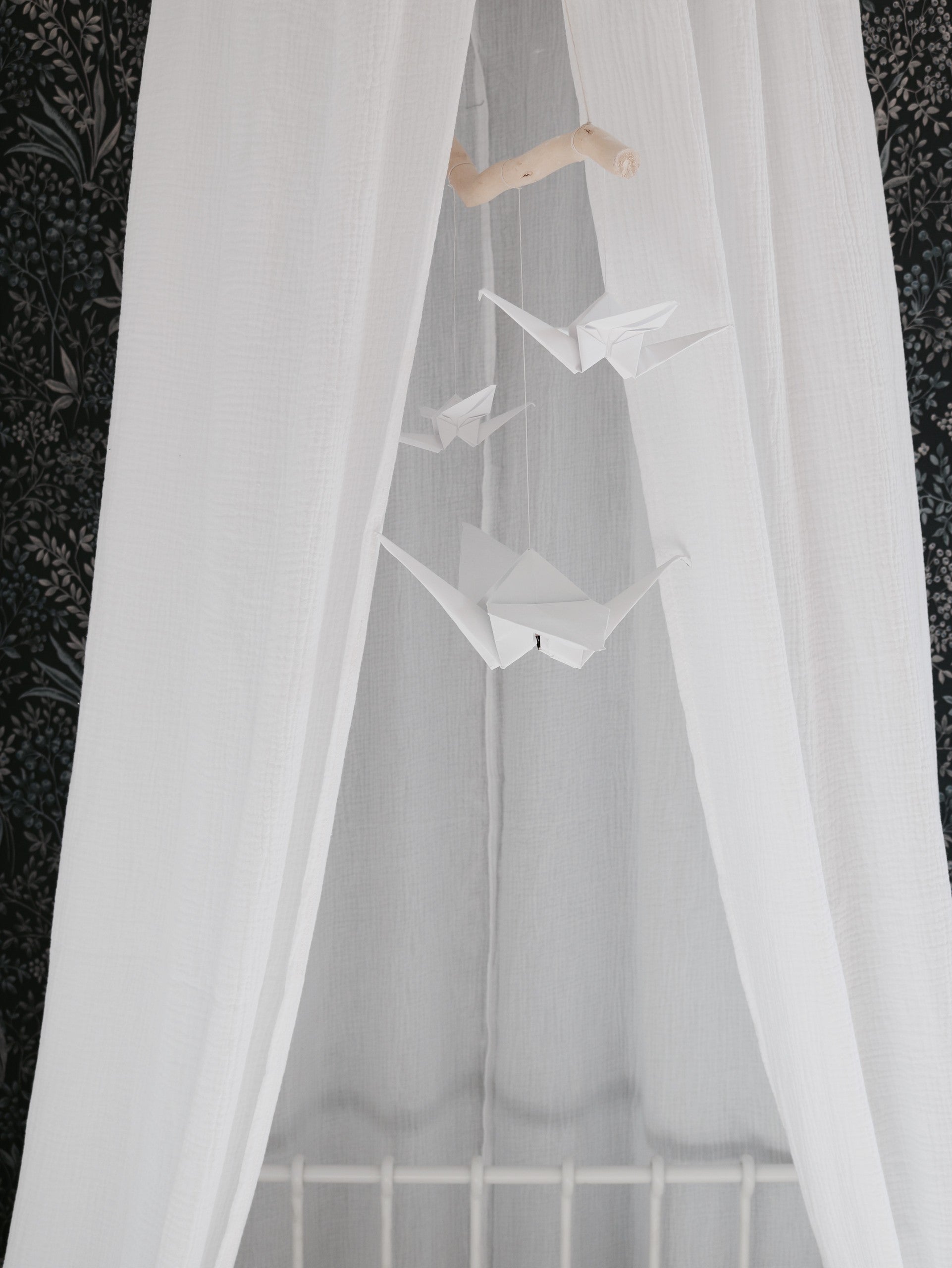 bold white origami nursery mobile with delicate cranes and pompoms, hanging above a crib in soft daylight