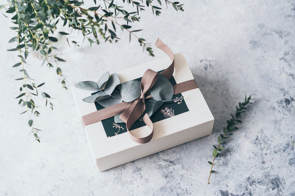 a contemporary leather gift box for women, open to reveal four vibrant natural body scrubs in warm, inviting light
