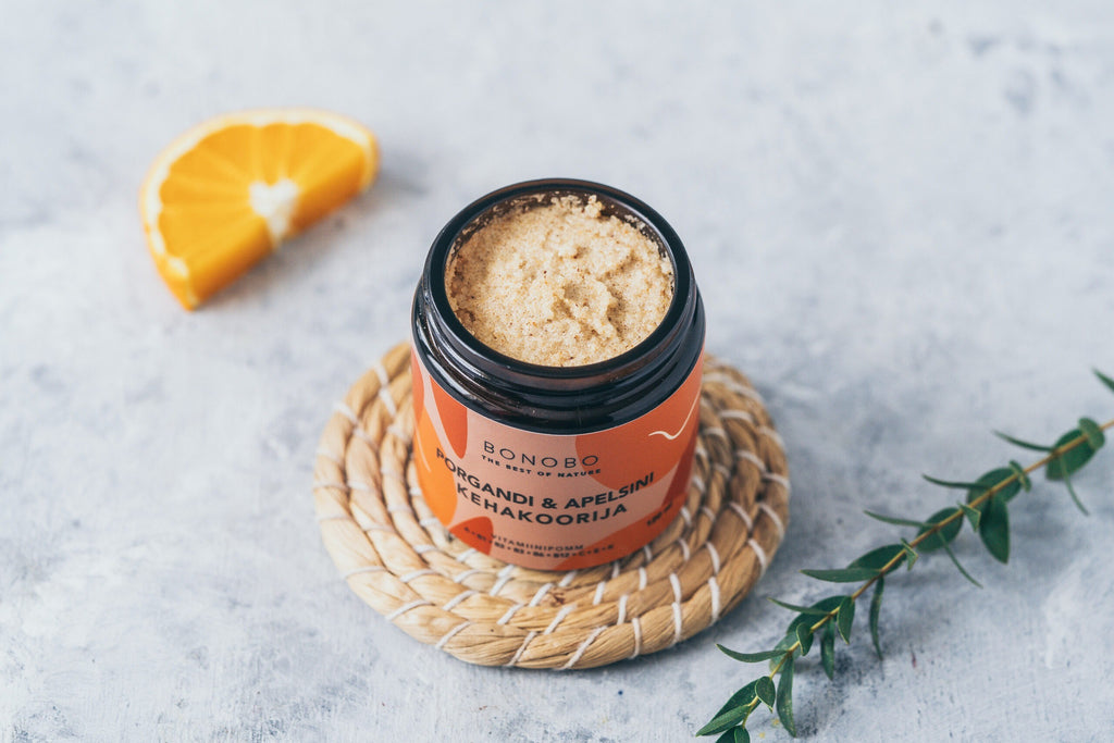 a contemporary leather gift box open to reveal four vibrant body scrubs in warm, inviting light