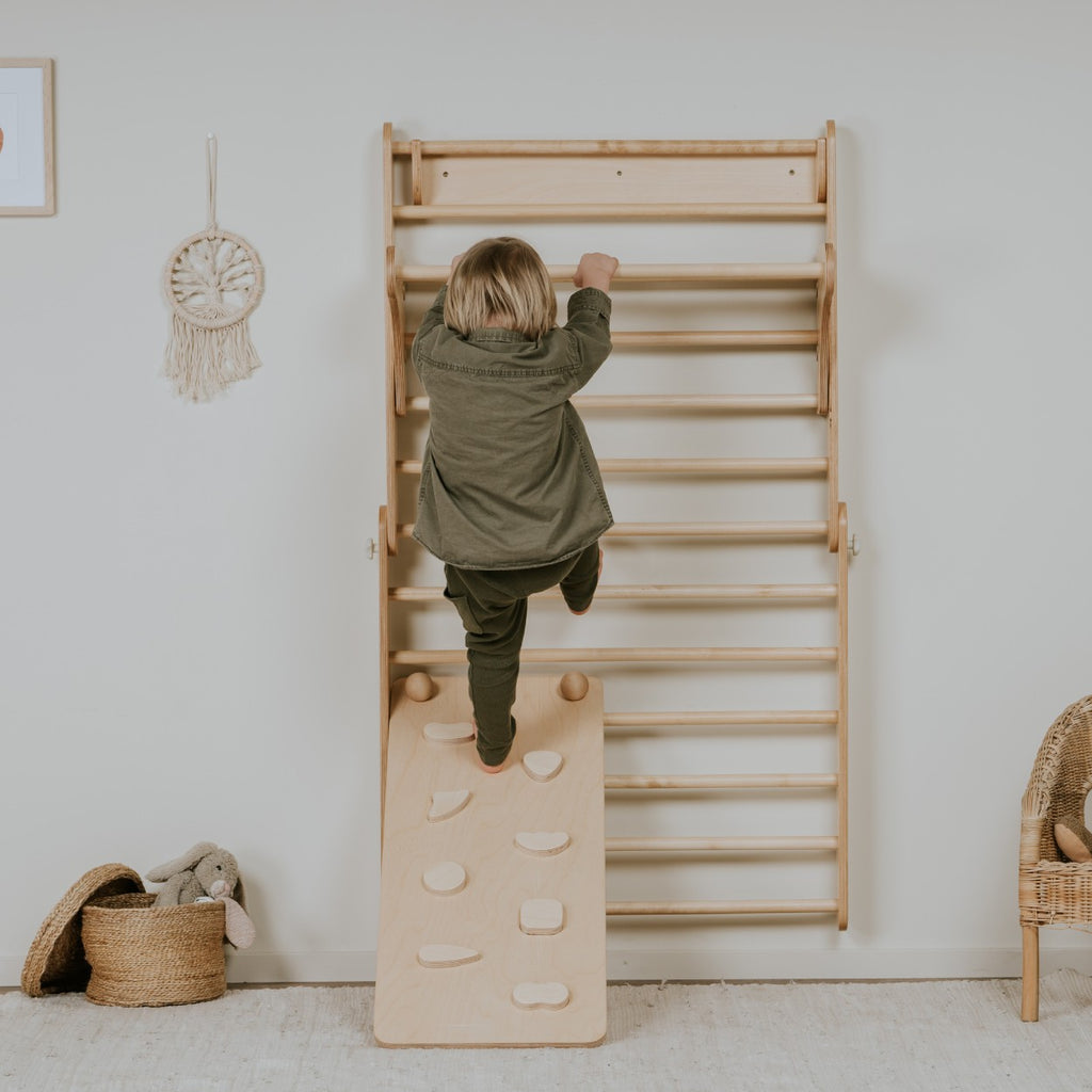 a bold toddler conquering the textured rock holds of a birch plywood climbing ramp