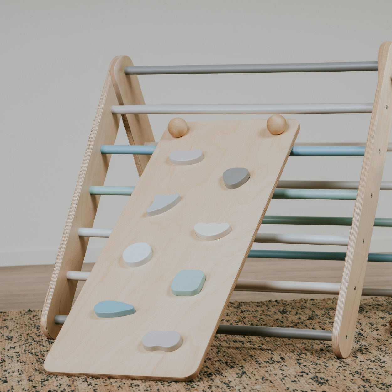 a pastel climbing ramp angled elegantly against a minimalist wall, showcasing its textured rock holds and refined birch wood finish