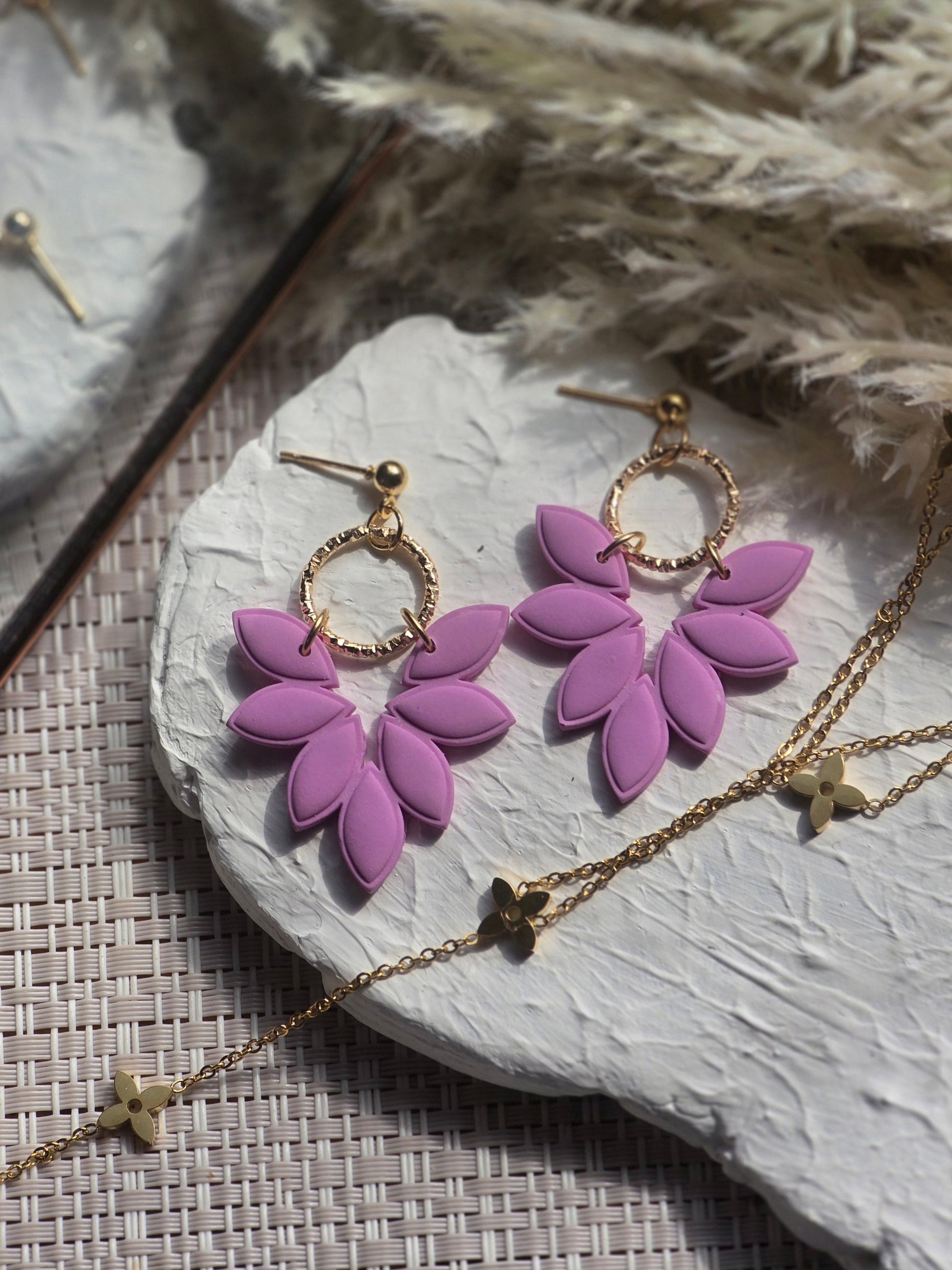 Purple floral earrings on a stone surface with a gold chain.
