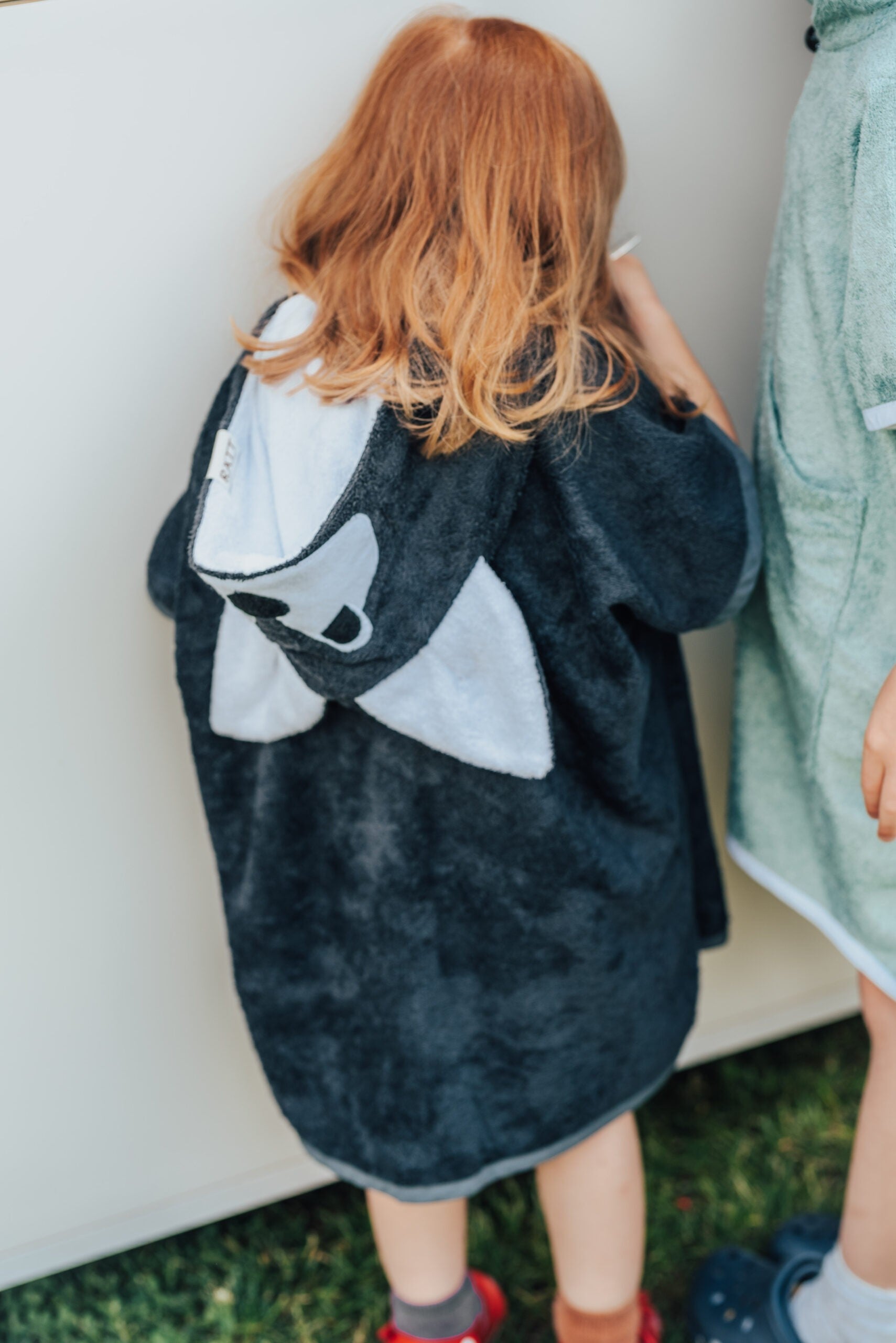 bold toddler in wolf poncho standing confidently on a rocky beach