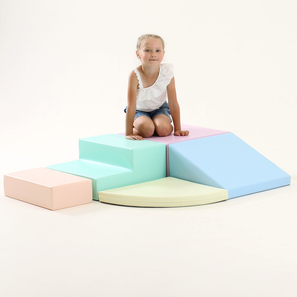 a child's hand reaching for a soft pastel foam corner climber block in warm morning light