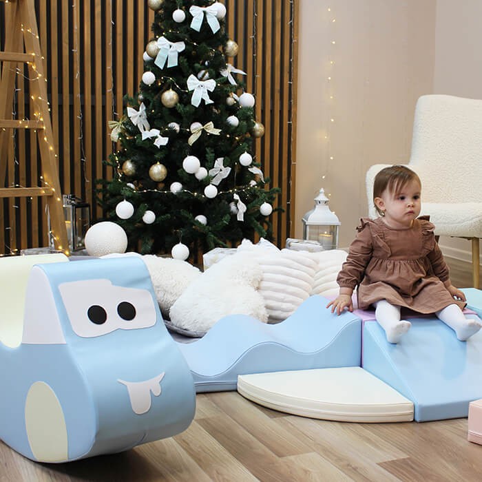 a child's hand guiding the light blue soft play car on a wooden floor