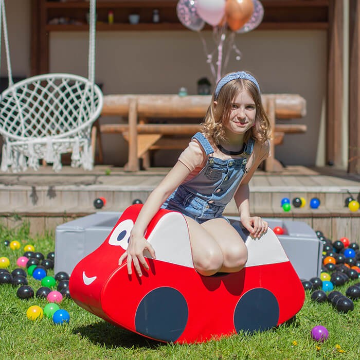 a soft red ride-on car for toddlers in a cozy, sunlit nursery setting