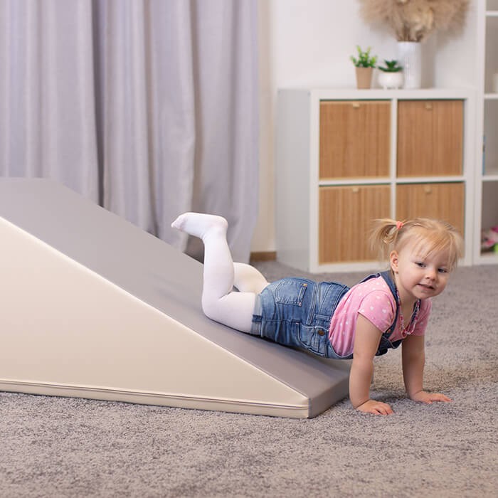 kids giggling on a beige and grey soft play slide set, climbing and sliding with joyful energy
