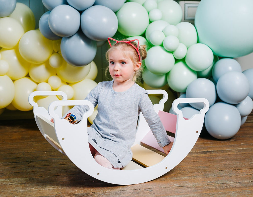 a child's hand on the vibrant rainbow climber, showcasing its smooth birch plywood texture and inviting play