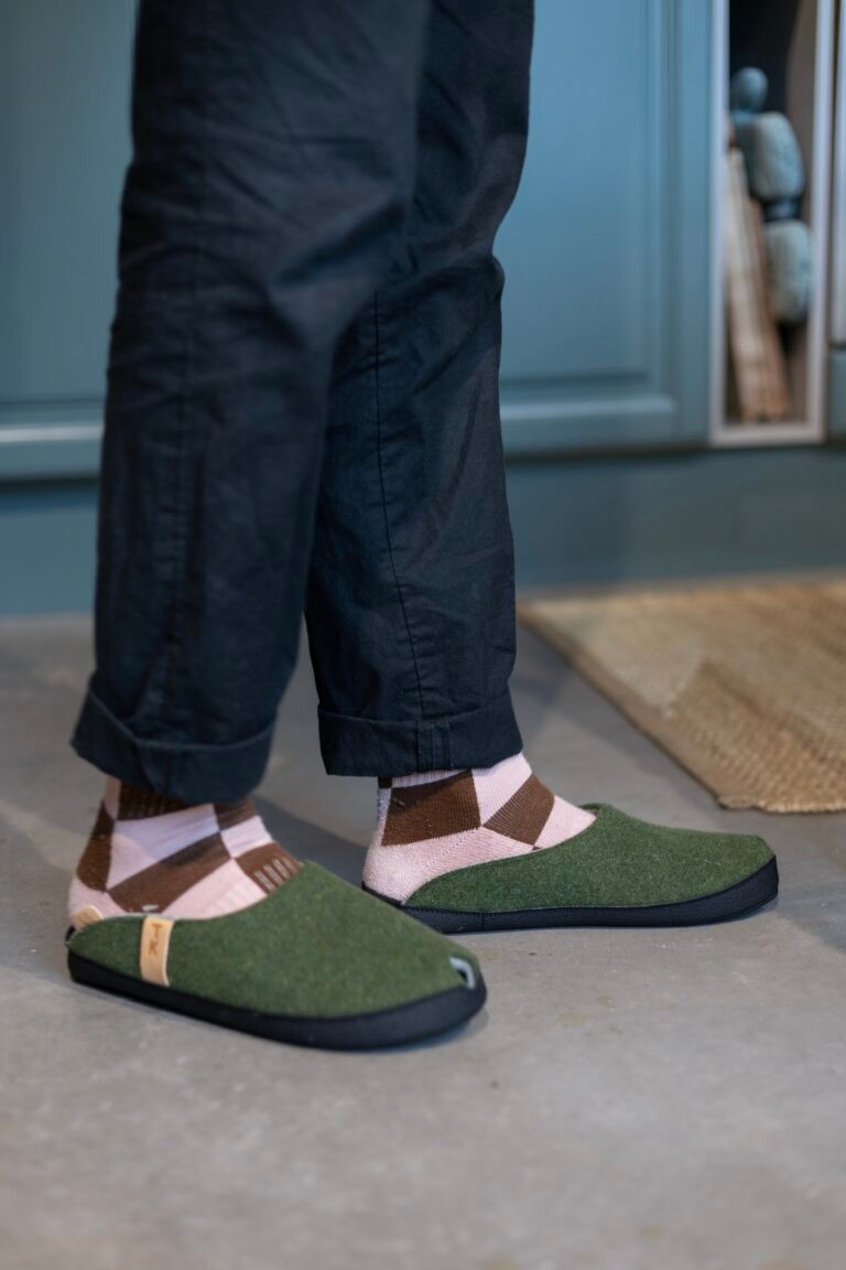 a soft moss green lambswool slipper resting on a cozy wool blanket