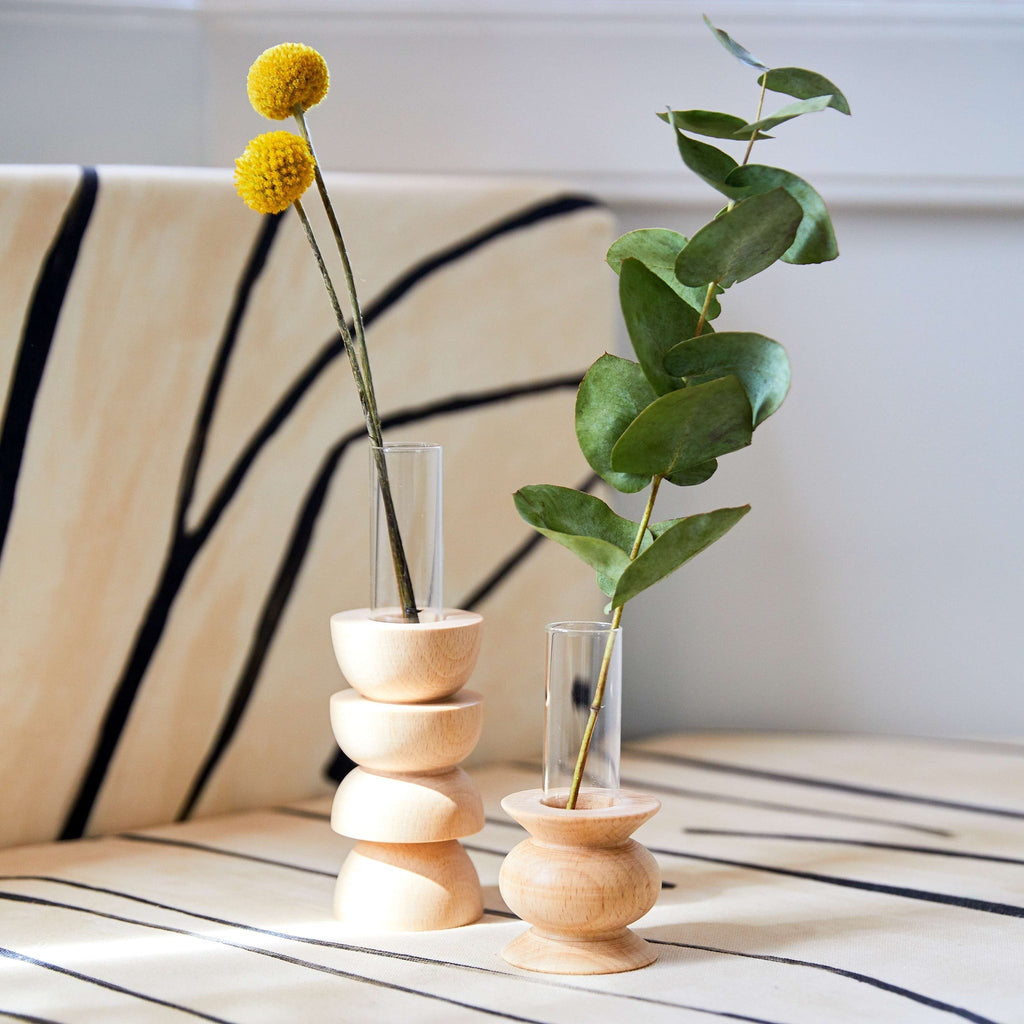 softly lit short totem wooden vase on a cozy table with a single stem in its glass insert