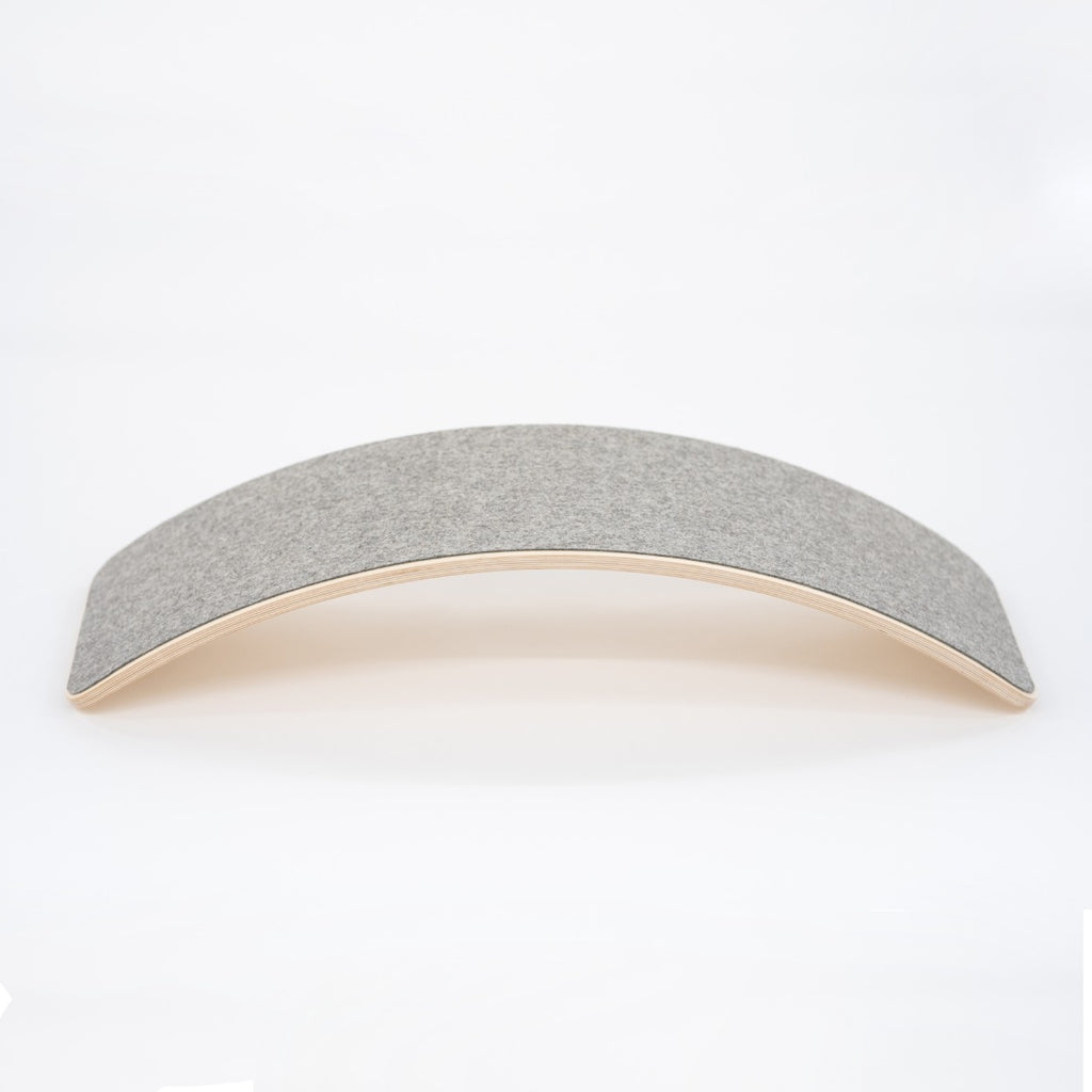a child gently rocking on a wooden balance board with soft grey felt in a cozy, sunlit room