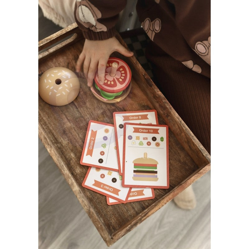 a child's small hands carefully placing a wooden lettuce slice on a stacked burger puzzle