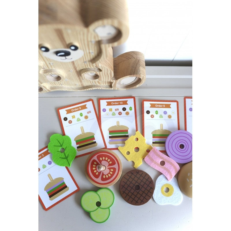 a child's hand stacking a sustainable wooden burger puzzle on a sunlit table