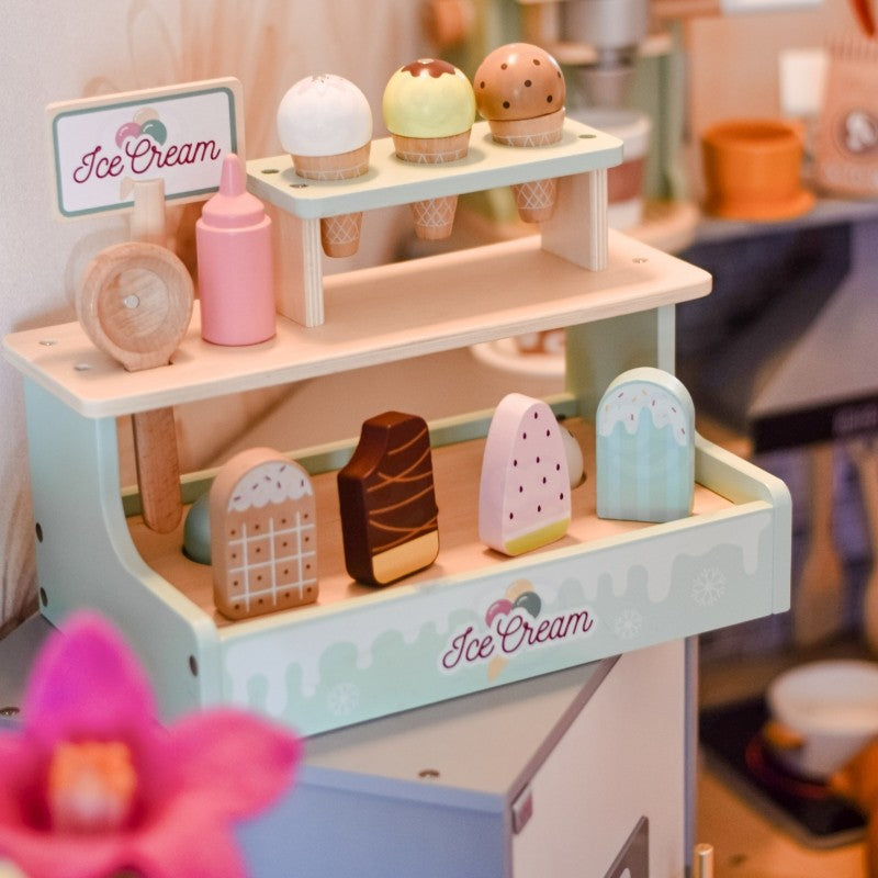 a child's hand carefully stacking a pink magnetic scoop on a wooden ice cream cone